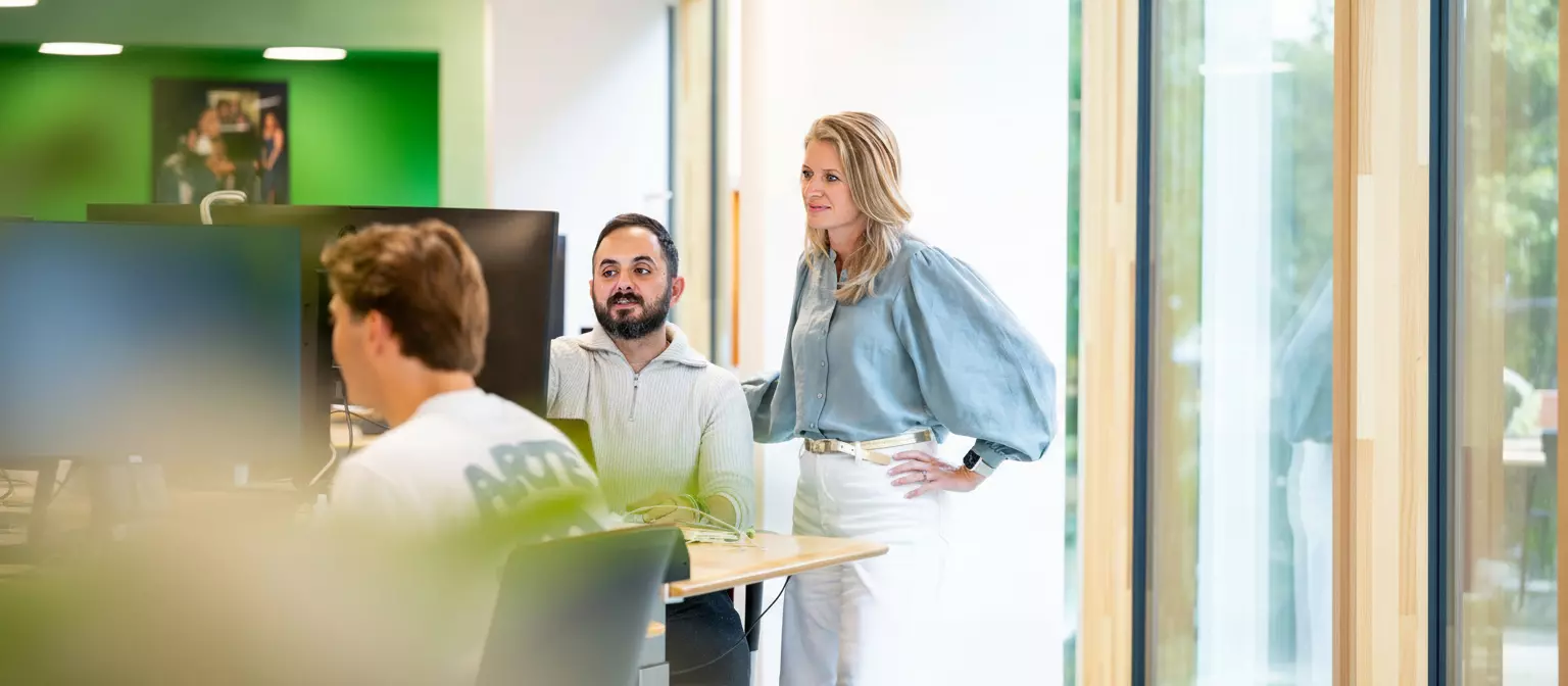 Drie collega's overleggen lachend op het kantoor van de Postcode Loterij.