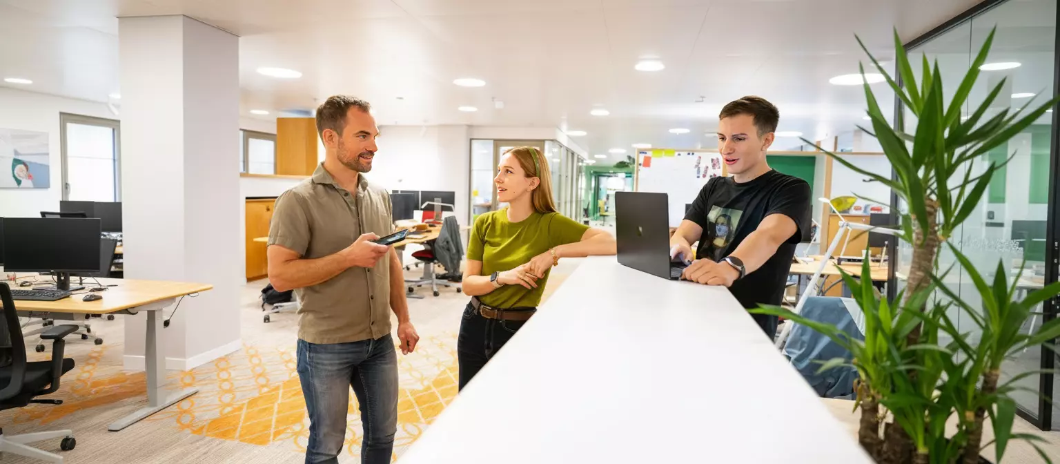 Medewerker van de Postcode Loterij achter de computer. Op de achtergrond zijn collega's aan het werk.